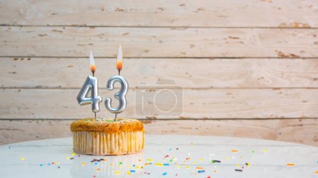Téléchargez les photos : Happy birthday greetings for 43 years of silver numbers on the background of white boards copy space. Beautiful birthday card with a muffin with a burning candle for forty-three years - en image libre de droit