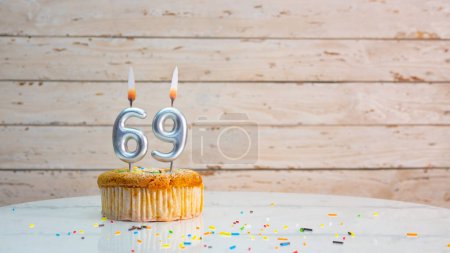 Foto de Happy 69th birthday greetings from silver numbers on white boards background copy space. Beautiful birthday card with a cupcake with a lit candle for sixty nine years - Imagen libre de derechos