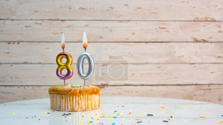 Happy 80th birthday greetings from silver numbers on white boards background copy space. Beautiful birthday card with a cupcake with a lit candle for eighty years