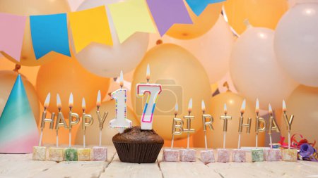 Photo for Happy birthday greetings for 17 years old from golden letters of candles burning against the background of mine space balloons. Beautiful birthday card with a muffin for seventeen years old - Royalty Free Image