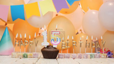Photo for Happy birthday greetings for a child of 15 years old from golden letters of candles burning against the background of mine space balloons. Beautiful birthday card with a muffin for fifteen years - Royalty Free Image