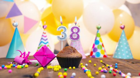 Foto de Happy birthday with a number of candles for thirty-eight years on the background of balloons. A festive muffin with burning candles and a pink gift box for a girl. Happy birthday for 38 years old girl. - Imagen libre de derechos