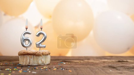 Téléchargez les photos : Happy birthday card with candle number 62 in a cupcake against the background of balloons. Copy space happy birthday for sixty two years old. - en image libre de droit