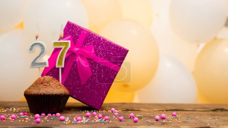 Téléchargez les photos : Happy birthday with a pink gift box for a 27 year old girl. Beautiful birthday card with a cupcake and a burning candle number twenty seven - en image libre de droit