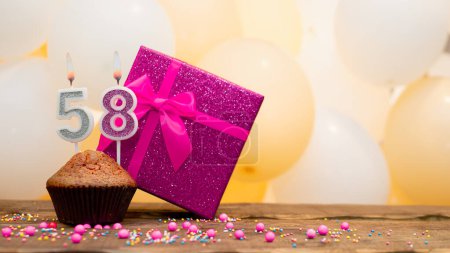 Happy birthday with a pink gift box for a 58 year old woman. Beautiful birthday card with a cupcake and a burning candle number fifty eight