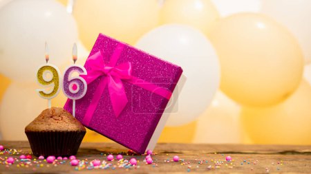Foto de Happy birthday with a pink gift box for a 96 year old woman. Beautiful birthday card with cupcake and burning candle number ninety six - Imagen libre de derechos