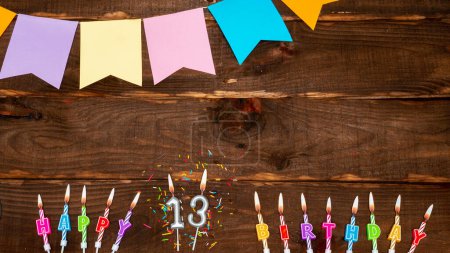 Photo for Top view, birthday decorations from letters of candles with fire and festive garlands, save space. Happy birthday background with number 13 on a brown board table. Happy birthday for a thirteen year old - Royalty Free Image