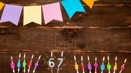 Photo for Top view, birthday decorations from letters of candles with fire and festive garlands, save space. Happy birthday background with number 67 on a brown board table. happy birthday to sixty seven - Royalty Free Image