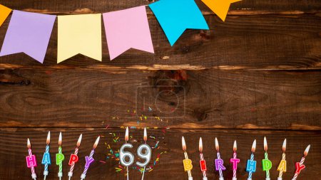 Foto de Top view, birthday decorations from letters of candles with fire and festive garlands, save space. Happy birthday background with number 69 on a brown board table. Happy birthday to sixty nine. - Imagen libre de derechos
