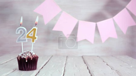 Birthday number 24. Festive background for a girl or woman with a muffin and candles burning pink in pastel colors with decorations for any holiday, copy space, women's gift boxes, place for text