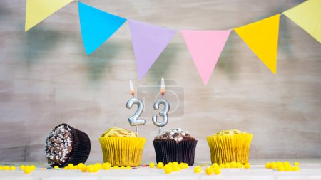 Téléchargez les photos : Birthday background with number 23. Beautiful birthday card with colorful garlands, a muffin with a candle burning copyspace - en image libre de droit