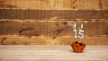 Foto de Scenery Festive wooden background happy birthday copy space. Anniversary background with number of burning candles and muffin. Beautiful brown from vintage boards background before a birthday with a number 15 - Imagen libre de derechos