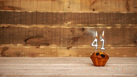 Foto de Scenery Festive wooden background happy birthday copy space. Anniversary background with number of burning candles and muffin. Beautiful brown from vintage boards background before a birthday with a number 41 - Imagen libre de derechos