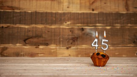 Foto de Scenery Festive wooden background happy birthday copy space. Anniversary background with number of burning candles and muffin. Beautiful brown from vintage boards background before a birthday with a number 45. - Imagen libre de derechos