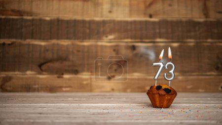 Foto de Scenery Festive wooden background happy birthday copy space. Anniversary background with number of burning candles and muffin. Beautiful brown from vintage boards background before a birthday with a number 73 - Imagen libre de derechos