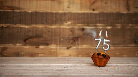 Foto de Scenery Festive wooden background happy birthday copy space. Anniversary background with number of burning candles and muffin. Beautiful brown from vintage boards background before a birthday with a number 75 - Imagen libre de derechos
