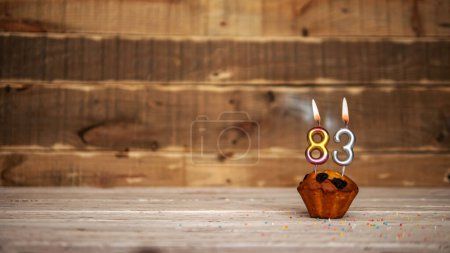 Foto de Scenery Festive wooden background happy birthday copy space. Anniversary background with number of burning candles and muffin. Beautiful brown from vintage boards background before a birthday with a number 83 - Imagen libre de derechos