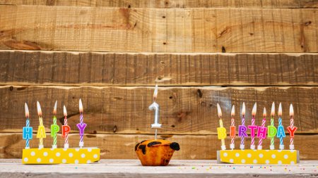 Photo for Muffin with a burning candle background for the anniversary on a beautiful wooden background. Postcard with letters of candles with congratulations for the holiday before the birthday. . Copy space. Happy birthday background 1 - Royalty Free Image