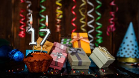 Foto de Birthday background with muffin and candles with number  17. Beautiful anniversary background with cake copy space with burning candles. Gift boxes with decorations. - Imagen libre de derechos
