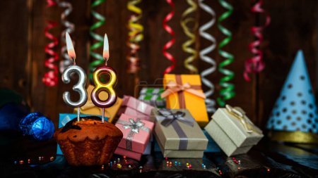 Foto de Birthday background with muffin and candles with number  38. Beautiful anniversary background with cake copy space with burning candles. Gift boxes with decorations. - Imagen libre de derechos