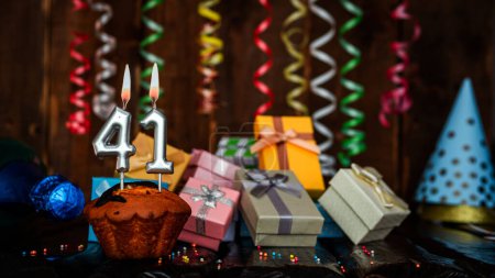Foto de Birthday background with muffin and candles with number  41. Beautiful anniversary background with cake copy space with burning candles. Gift boxes with decorations. - Imagen libre de derechos