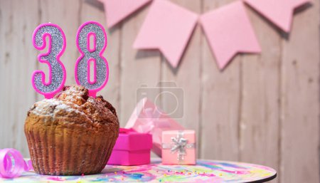 Foto de Festive cake or muffin with a pink candle with a number  38. Happy birthday background with a number for a girl or woman with beautiful decorations. Anniversary party copy space. - Imagen libre de derechos