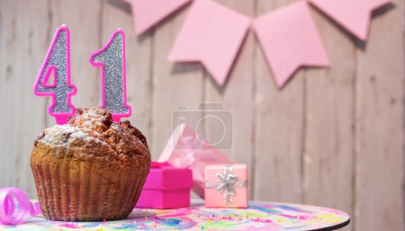 Foto de Festive cake or muffin with a pink candle with a number  41. Happy birthday background with a number for a girl or woman with beautiful decorations. Anniversary party copy space. - Imagen libre de derechos
