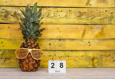 Creative May calendar planner with number  28. Pineapple character on bright yellow summer wooden background with calendar cubes.
