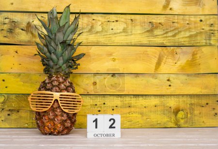 Foto de Creative october calendar planner with number  12. Pineapple character on bright yellow summer wooden background with calendar cubes. - Imagen libre de derechos