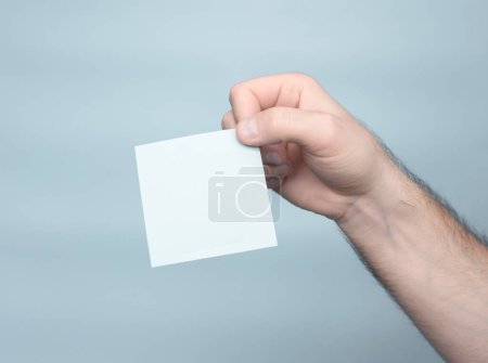 Foto de A man's hand holds a sticker blank for your text inscription. Message on sticker copy space. Mini banner for text in a person's hand. On a light pastel background - Imagen libre de derechos