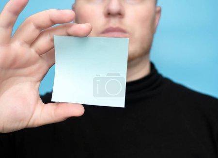 Foto de A young man is holding a sticker blank for the inscription of your text. Message on sticker copy space. Mini banner for text in a person's hand. On a light pastel background - Imagen libre de derechos