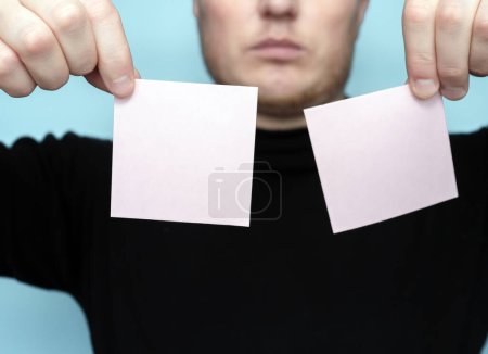 Foto de A young man is holding two blank stickers for the inscription of your text. Message on sticker copy space. Mini banner for text in a person's hand. On a light pastel background - Imagen libre de derechos