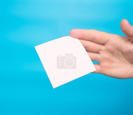 Foto de A hand holds a blank letter sticker for your text inscription. Message on sticker copy space. Mini banner for text in a person's hand. On a light pastel background - Imagen libre de derechos