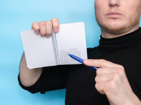 Foto de A hand holds a sticker notepad with a pen, an empty space for a free letter to inscribe your text. Message on sticker copy space. Mini banner for text in a person's hand. On a pastel blue background - Imagen libre de derechos