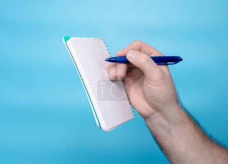 Foto de A man's hand holds a notepad notepad sticker with a pen, a free letter space for inscription of your text. Message on sticker copy space. Mini banner for text in a person's hand. On a pastel blue background - Imagen libre de derechos