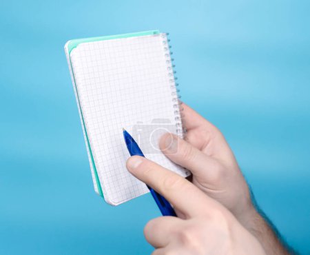Foto de A man's hand holds a sticker notepad with a pen, a free letter space for inscription of your text. Message on sticker copy space. Mini banner for text in a person's hand. On a pastel blue background - Imagen libre de derechos