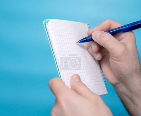 Foto de The hand of a young man holds a notepad sticker notepad with a pen, a free letter space for inscription of your text. Message on sticker copy space. Mini banner for text in a person's hand. On a pastel blue background - Imagen libre de derechos