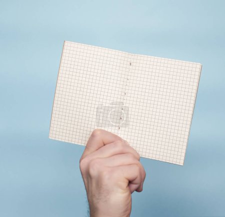 Foto de Studio shot Blank notebook in a cage for text in the hands of a young man on a blue background. Notes copy space. Place for text banner notepad. write a message in notepad - Imagen libre de derechos