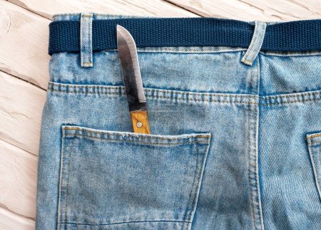 Téléchargez les photos : Couteau vue de dessus dans la poche du pantalon. Un couteau tranchant dans une poche de jeans. - en image libre de droit