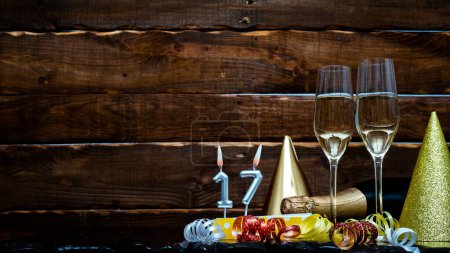 Photo for Solemn background for the anniversary with the number  17. Happy birthday background on brown wooden background with champagne bottle and champagne glasses. Beautiful holiday decorations copy space. - Royalty Free Image
