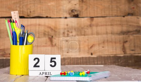 Téléchargez les photos : Calendrier d'avril avec le numéro 25. Stylos et crayons de papeterie dans une boîte sur un fond vintage en bois. Bloc-notes d'espace de copie avec crayons et calendrier. Place du planificateur pour le texte. - en image libre de droit