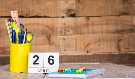 Photo for April calendar background with number  26. Stationery pens and pencils in a case on a wooden vintage background. Copy space notepad with pencils and calendar. Planner place for text. - Royalty Free Image