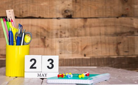 May calendar background with number  23. Stationery pens and pencils in a case on a wooden vintage background. Copy space notepad with pencils and calendar. Planner place for text.