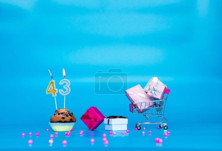 Téléchargez les photos : Carte créative Joyeux anniversaire pour une fille ou une femme avec un certain nombre de bougies dans une tarte aux muffins 43. Joyeux anniversaire boîtes cadeaux dans les tons roses. Anniversaire de l'espace de copie de fond sur fond bleu. - en image libre de droit