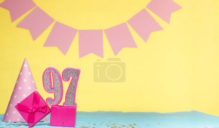 Date of birth for a girl  97. Copy space. Birthday in pink shades with a yellow background. Decorations with numbered candles and a gift box. Anniversary card for a woman