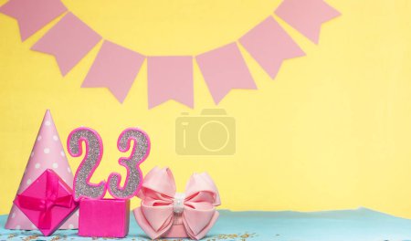 Date of birth for a girl  23. Copy space. Birthday in pink shades with a yellow background. Decorations with numbered candles and a gift box. Anniversary card for a woman