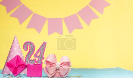 Foto de Fecha de nacimiento para una niña 24. Copiar espacio. Cumpleaños en tonos rosados con un fondo amarillo. Decoraciones con velas numeradas y una caja de regalo. Tarjeta de aniversario para una mujer - Imagen libre de derechos
