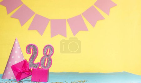 Date of birth for a girl  28. Copy space. Birthday in pink shades with a yellow background. Decorations with numbered candles and a gift box. Anniversary card for a woman