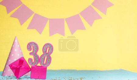 Fecha de nacimiento para una niña 38. Copiar espacio. Cumpleaños en tonos rosados con un fondo amarillo. Decoraciones con velas numeradas y una caja de regalo. Tarjeta de aniversario para una mujer