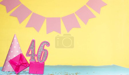 Fecha de nacimiento para una niña 46. Copiar espacio. Cumpleaños en tonos rosados con un fondo amarillo. Decoraciones con velas numeradas y una caja de regalo. Tarjeta de aniversario para una mujer